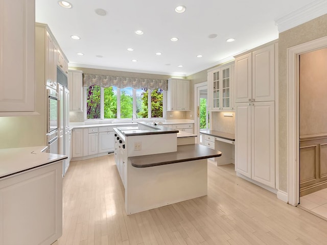 kitchen with white cabinets, a kitchen island, ornamental molding, and light hardwood / wood-style flooring