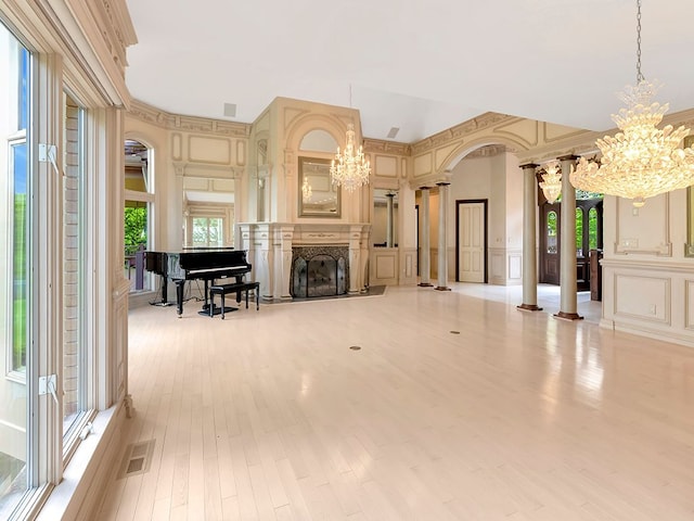 living room with ornate columns, ornamental molding, light hardwood / wood-style flooring, a notable chandelier, and a fireplace