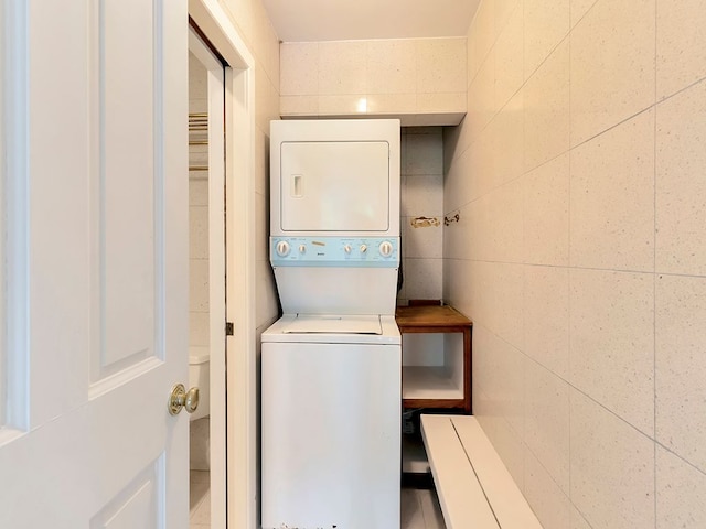 clothes washing area featuring stacked washing maching and dryer and tile walls