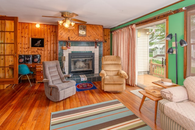 living room featuring a tiled fireplace, wood walls, ceiling fan, and hardwood / wood-style flooring