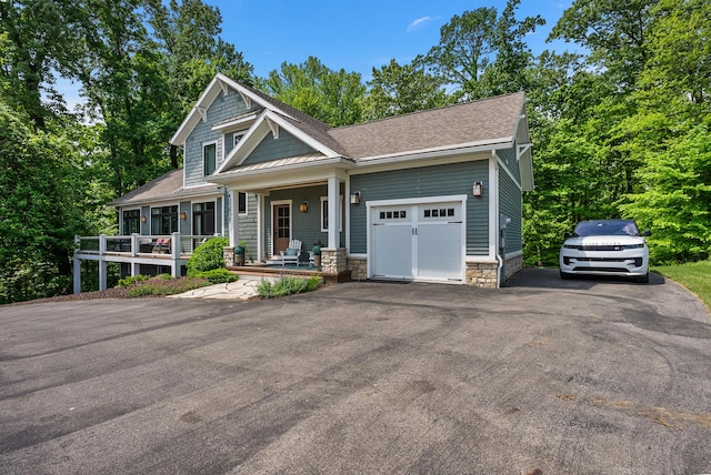 view of front of property featuring aphalt driveway, a porch, a shingled roof, a garage, and stone siding