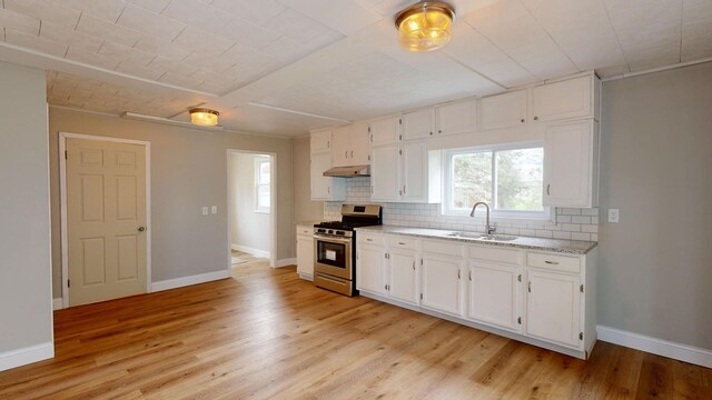 7200 E Tomah Rd, Mount Pleasant, MI 48858 - kitchen with gas range, a sink, under cabinet range hood, decorative backsplash, and baseboards