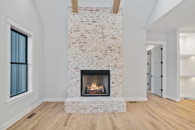 unfurnished living room featuring lofted ceiling with beams, a fireplace, visible vents, and wood finished floors