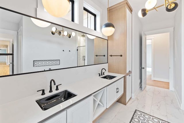 full bath featuring marble finish floor, double vanity, a sink, and baseboards