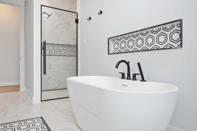 bathroom featuring marble finish floor, a freestanding tub, a marble finish shower, and baseboards