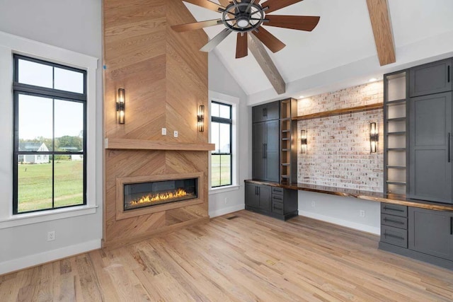 unfurnished living room featuring a glass covered fireplace, light wood-type flooring, built in study area, and a wealth of natural light