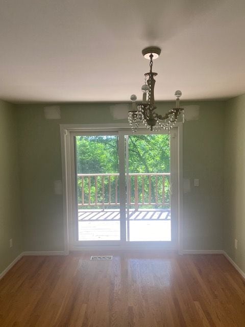 empty room with wood-type flooring and a notable chandelier