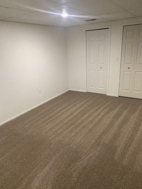 unfurnished bedroom featuring dark carpet and a drop ceiling