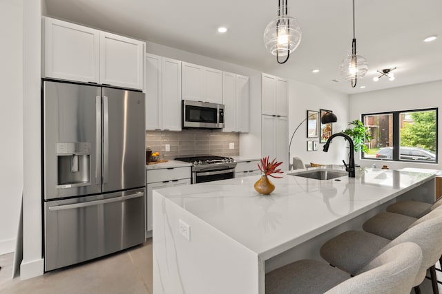 kitchen featuring light stone countertops, sink, stainless steel appliances, a kitchen island with sink, and white cabinets