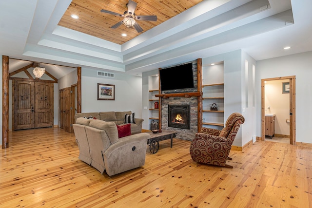 living room with built in shelves, light wood-type flooring, a tray ceiling, and ceiling fan