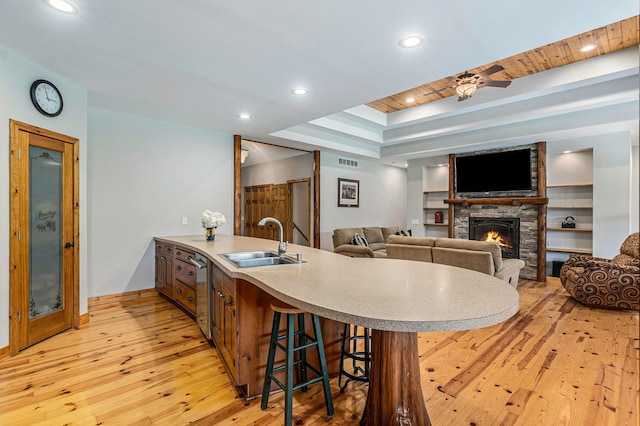 kitchen with ceiling fan, sink, a raised ceiling, a fireplace, and light wood-type flooring