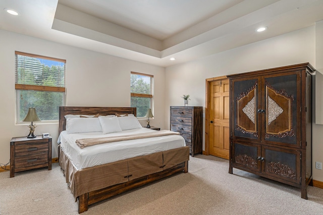 carpeted bedroom featuring a tray ceiling and multiple windows