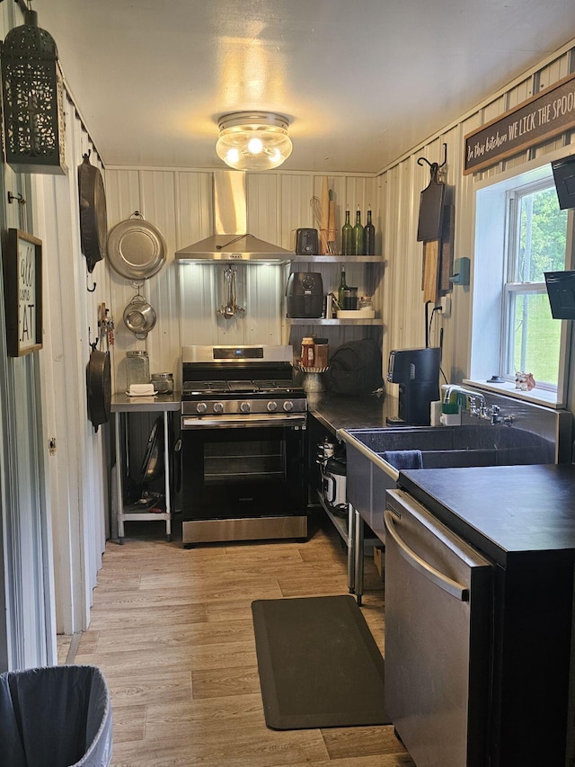 kitchen with appliances with stainless steel finishes, light wood-type flooring, and wall chimney range hood