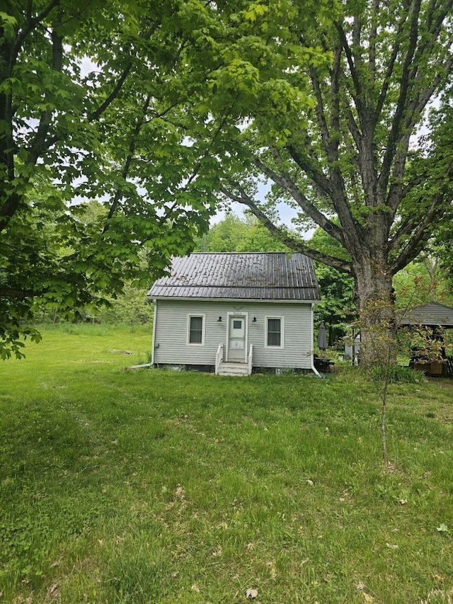 rear view of house featuring entry steps, metal roof, and a yard