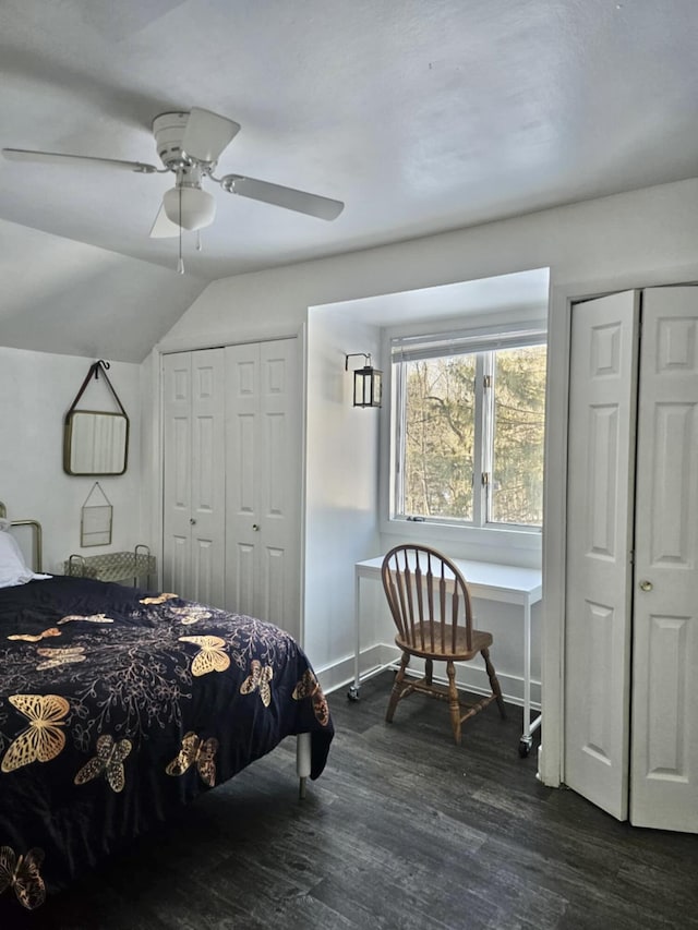 bedroom with baseboards, a ceiling fan, dark wood-style flooring, vaulted ceiling, and two closets