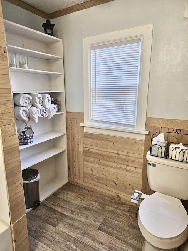 interior space with a wainscoted wall, crown molding, toilet, wood walls, and wood finished floors