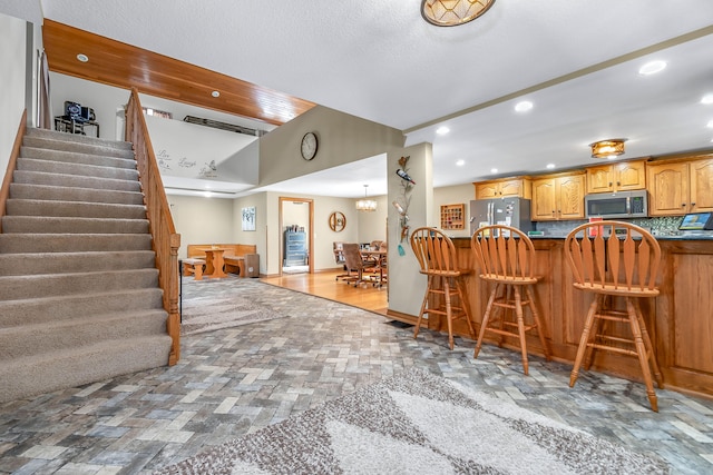 kitchen featuring hardwood / wood-style floors, a breakfast bar area, decorative backsplash, stainless steel appliances, and a chandelier