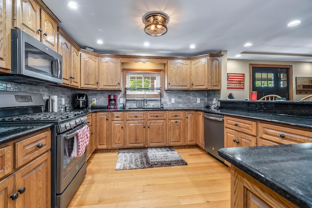 kitchen featuring backsplash, stainless steel appliances, light hardwood / wood-style floors, and dark stone countertops