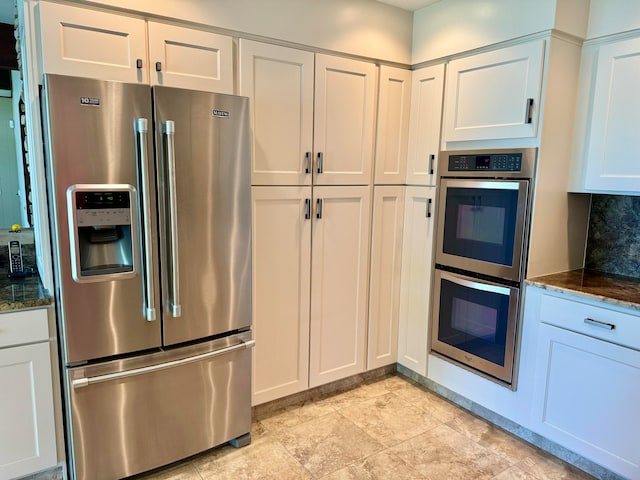 kitchen featuring white cabinetry, backsplash, appliances with stainless steel finishes, and dark stone counters