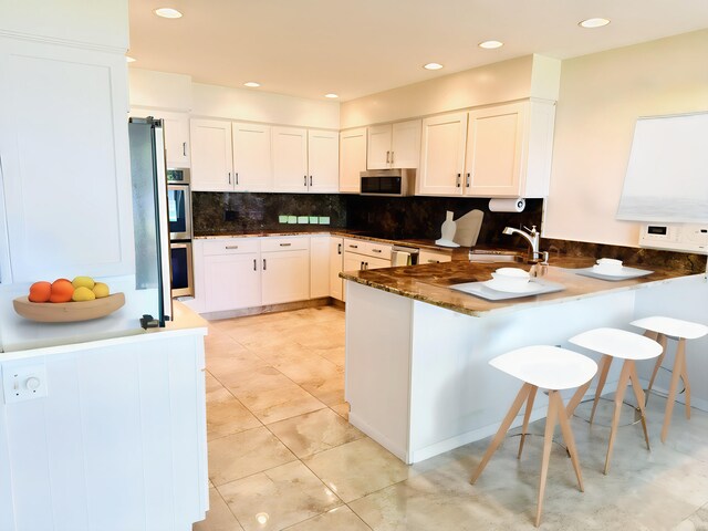 7206 Beechwood Cir, Watervliet, MI 49098 - kitchen with a peninsula, stainless steel appliances, tasteful backsplash, a sink, and white cabinets