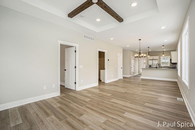 unfurnished living room with beamed ceiling, light wood-type flooring, an inviting chandelier, and sink