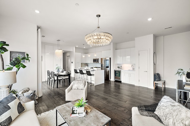 living room featuring a notable chandelier, dark hardwood / wood-style floors, sink, and wine cooler