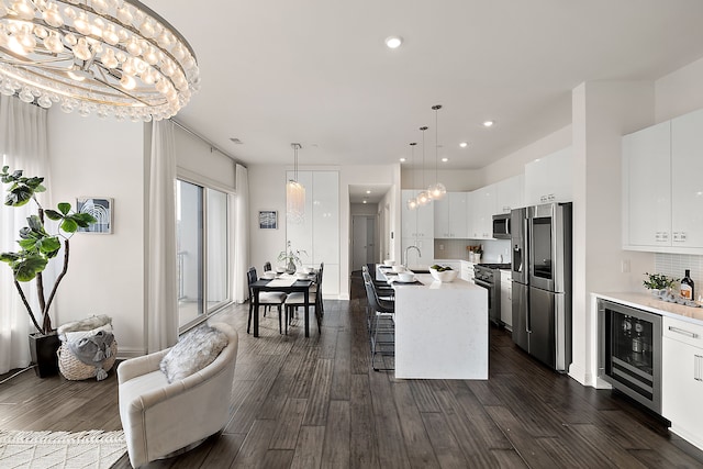 kitchen featuring appliances with stainless steel finishes, white cabinetry, a chandelier, wine cooler, and an island with sink