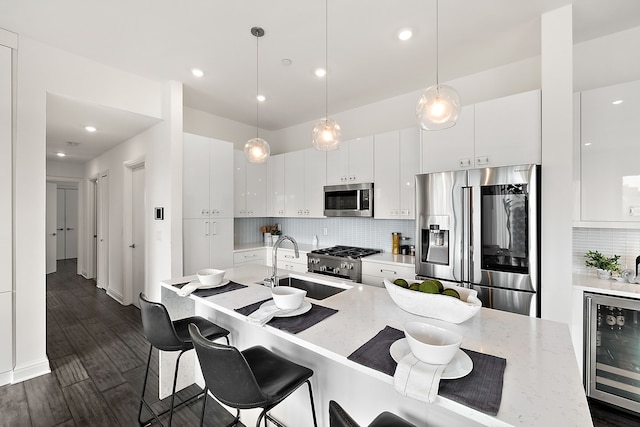 kitchen with appliances with stainless steel finishes, dark hardwood / wood-style flooring, beverage cooler, decorative light fixtures, and white cabinets