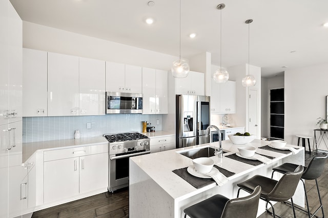 kitchen with a breakfast bar, a kitchen island with sink, appliances with stainless steel finishes, a sink, and backsplash