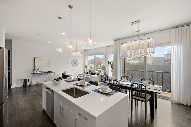 kitchen with a chandelier, a kitchen island with sink, appliances with stainless steel finishes, dark wood finished floors, and a sink