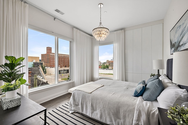 bedroom with multiple windows, visible vents, wood finished floors, and a chandelier