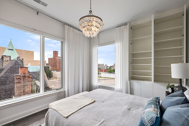 bedroom with visible vents, a chandelier, baseboards, wood finished floors, and a view of city