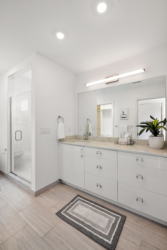 bathroom featuring a shower stall, baseboards, double vanity, recessed lighting, and a sink