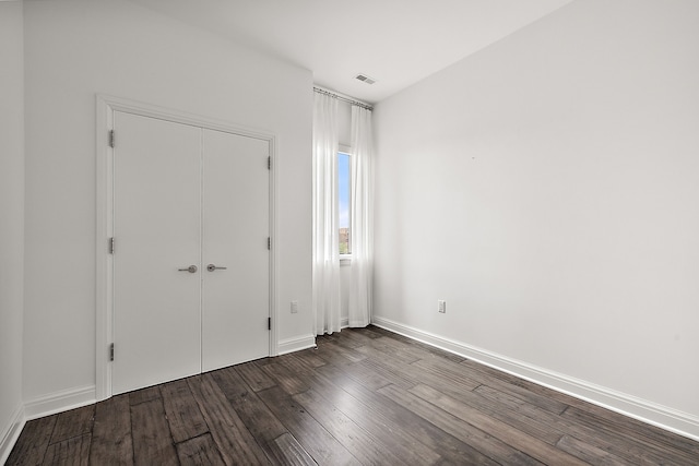 unfurnished bedroom with a closet, dark wood-style flooring, visible vents, and baseboards