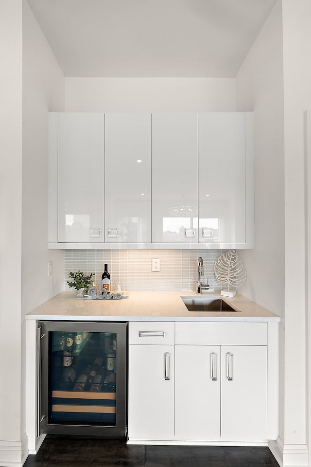 bar with bar area, baseboards, backsplash, a sink, and beverage cooler
