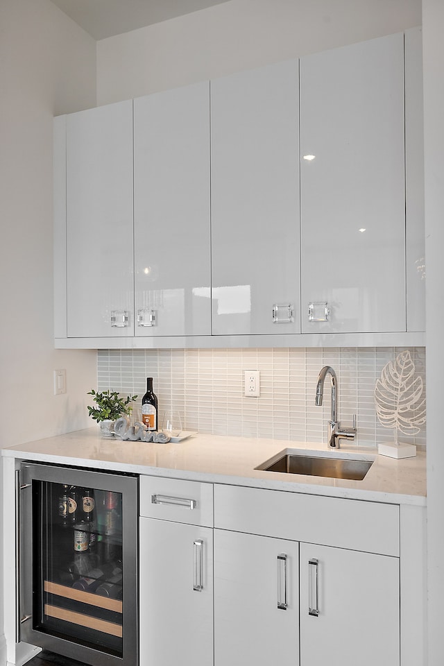 bar featuring white cabinetry, sink, beverage cooler, and tasteful backsplash