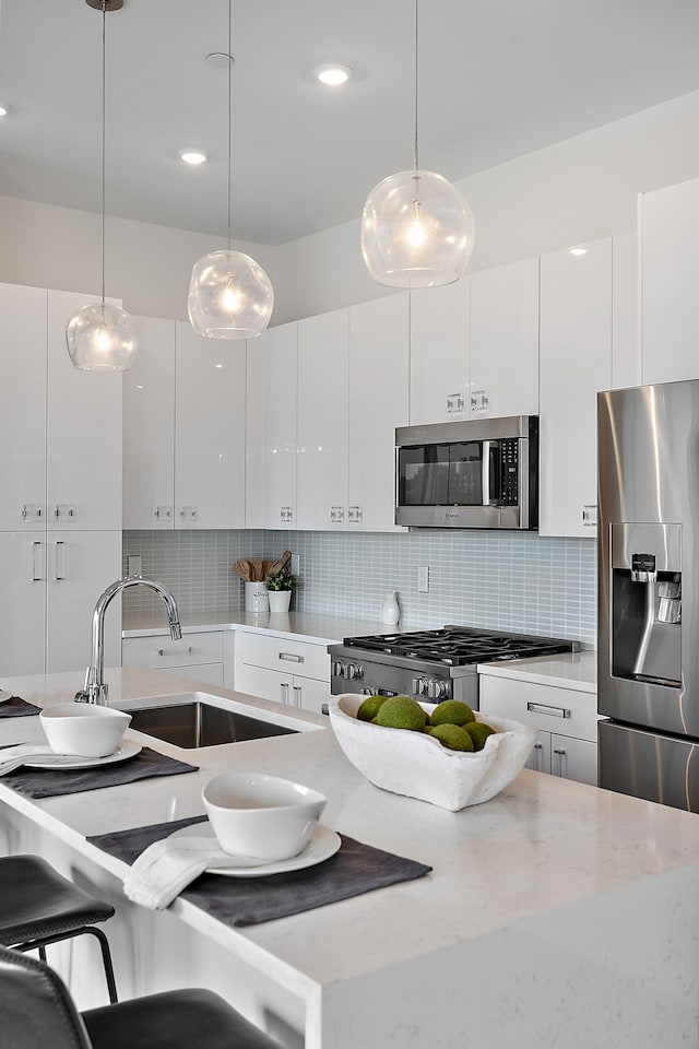 kitchen with decorative light fixtures, white cabinetry, stainless steel appliances, and tasteful backsplash