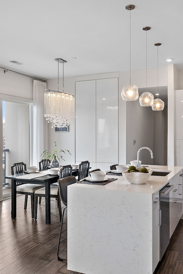 kitchen with pendant lighting, a kitchen island with sink, sink, dark hardwood / wood-style floors, and white cabinetry