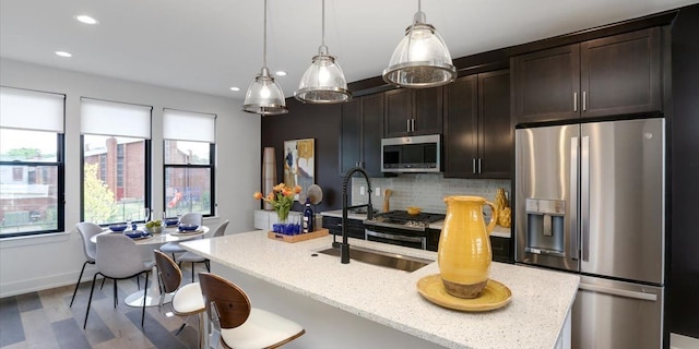 kitchen featuring backsplash, dark brown cabinetry, decorative light fixtures, wood-type flooring, and stainless steel appliances