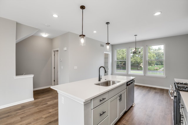 kitchen with sink, hardwood / wood-style floors, decorative light fixtures, a kitchen island with sink, and appliances with stainless steel finishes