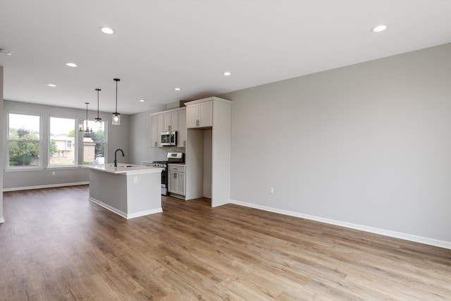 kitchen featuring pendant lighting, a kitchen island with sink, white cabinets, light hardwood / wood-style flooring, and stainless steel appliances