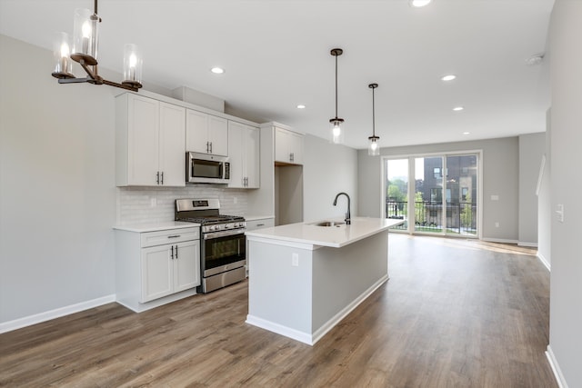 kitchen with appliances with stainless steel finishes, a center island with sink, hanging light fixtures, and sink