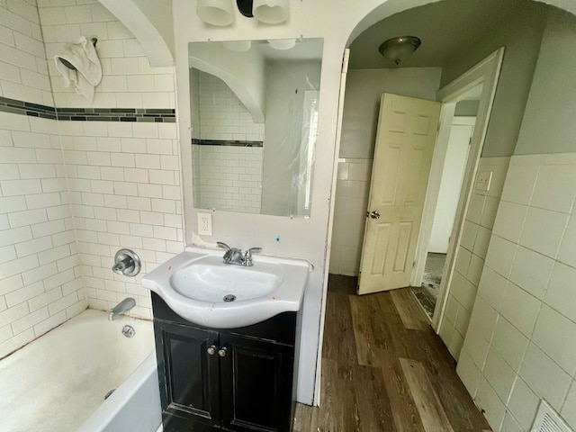 bathroom with hardwood / wood-style floors, vanity, tile walls, and tiled shower / bath combo