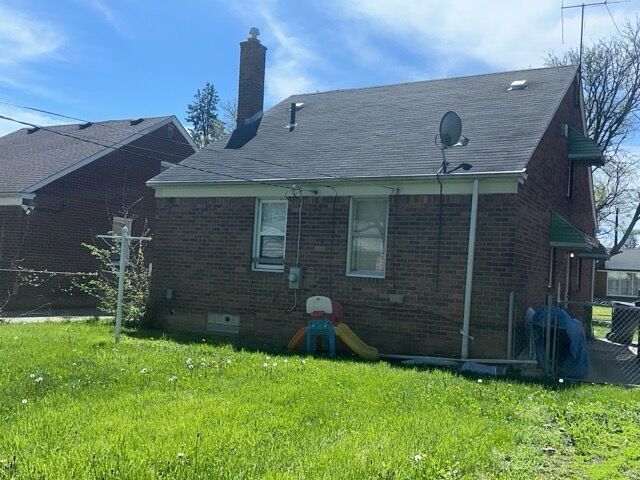 14141 Rossini Dr, Detroit, MI 48205 - rear view of house featuring a chimney, brick siding, and a yard