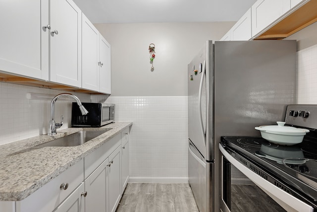 kitchen featuring light stone countertops, appliances with stainless steel finishes, light wood-type flooring, sink, and white cabinetry