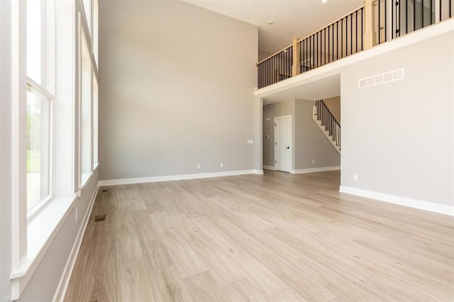 unfurnished living room featuring light wood-type flooring and a towering ceiling