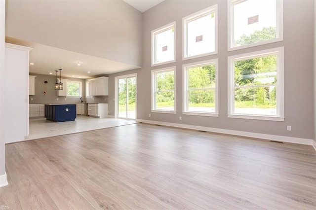 unfurnished living room with light hardwood / wood-style floors and a towering ceiling