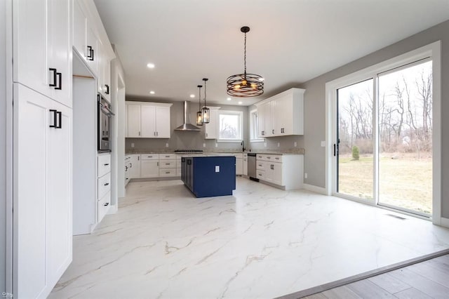 kitchen featuring white cabinets, wall chimney exhaust hood, a center island, and decorative light fixtures