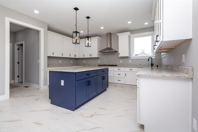 kitchen featuring a center island, white cabinets, blue cabinets, hanging light fixtures, and wall chimney exhaust hood