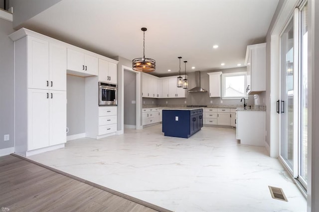 kitchen featuring wall chimney exhaust hood, appliances with stainless steel finishes, decorative light fixtures, a kitchen island, and white cabinetry